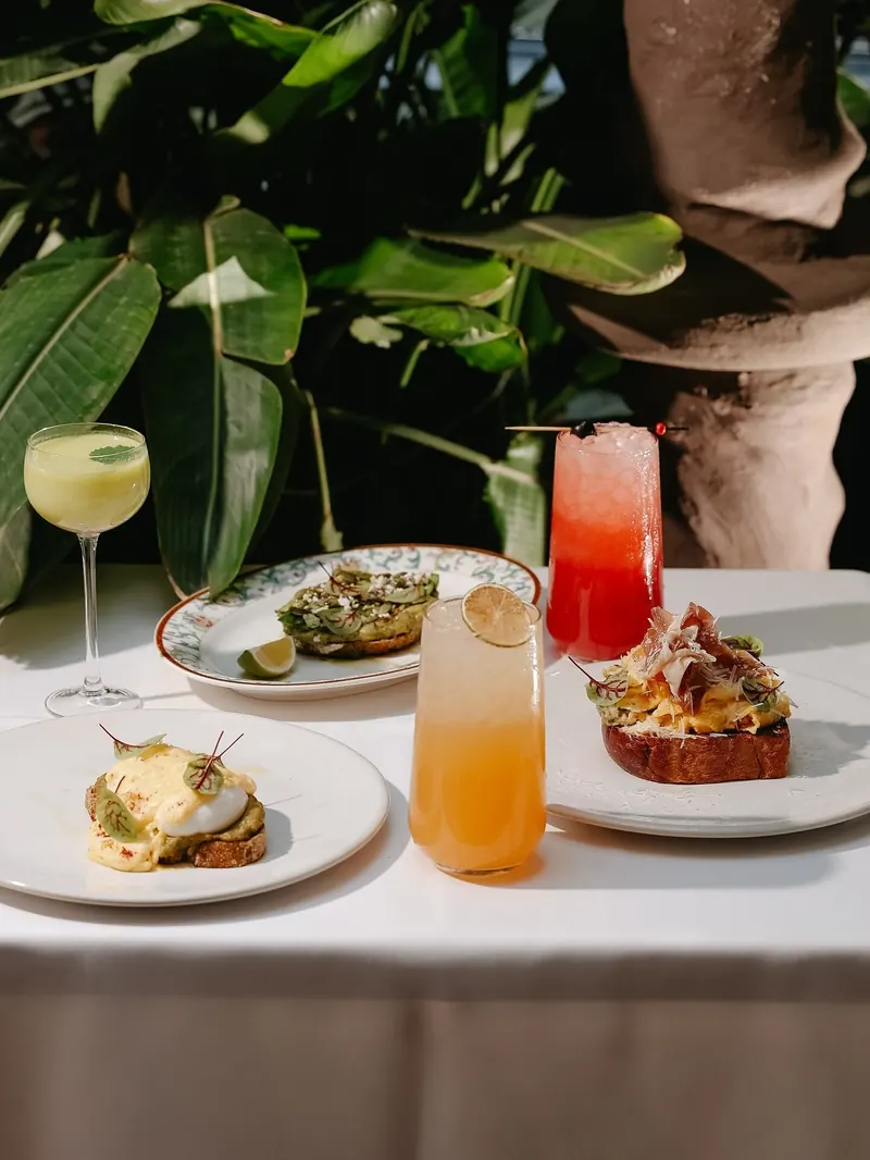 Breakfast plates and fresh drinks on a white tablecloth among jungle leaves