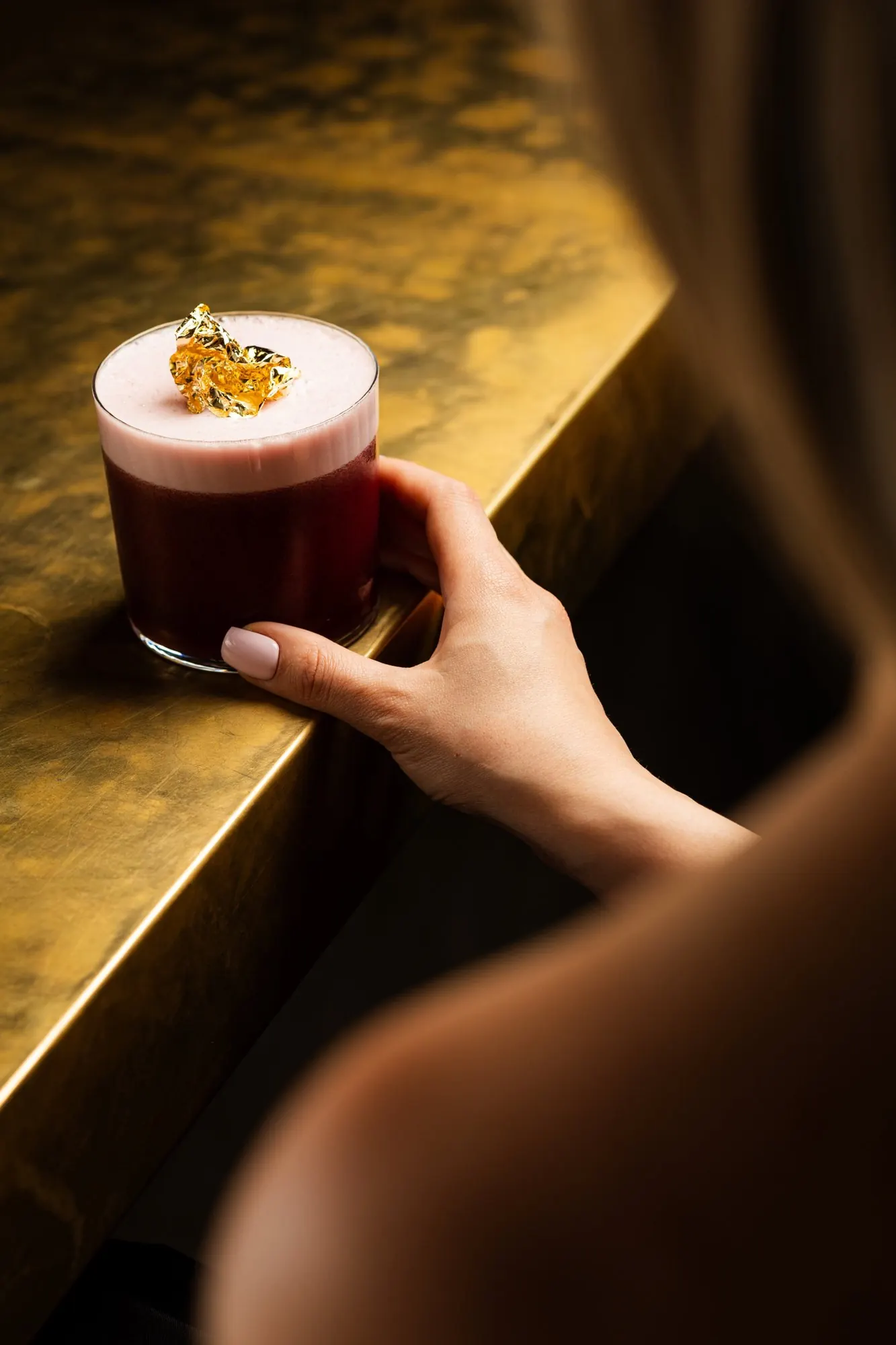 A cocktail topped with gold leaf on the gold bar counter