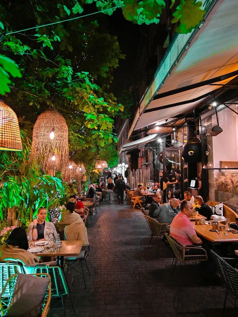 The terrace at night under the trees, with rattan lamps and guests at the tables