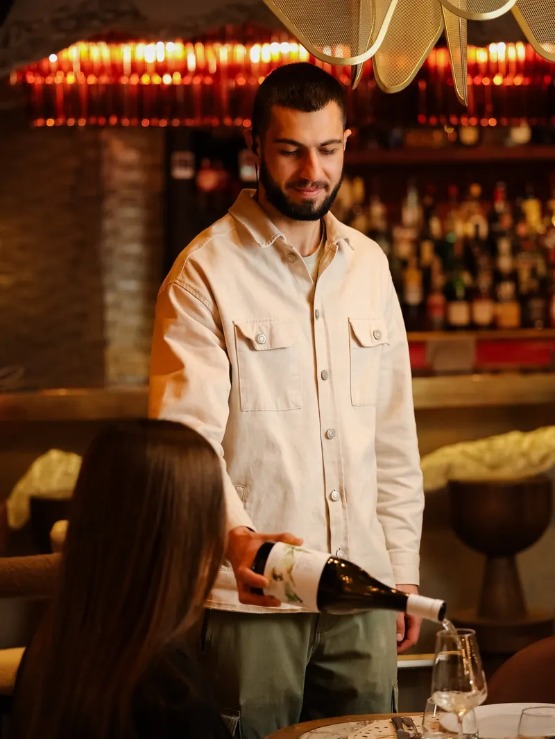 Wine being poured at the table, the bar shelves behind